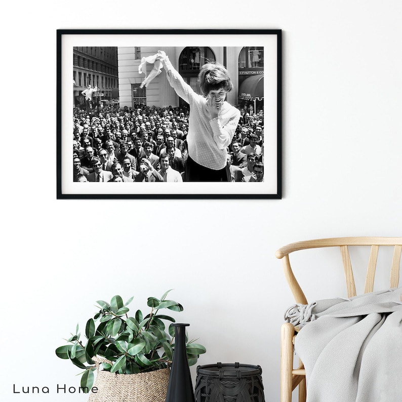 Puede incluir: Impresi&oacute;n enmarcada en blanco y negro que muestra a una mujer levantando una prenda frente a una gran multitud. La fotograf&iacute;a captura un momento de celebraci&oacute;n o triunfo, con una est&eacute;tica vintage. El fondo incluye edificios y una escena callejera.