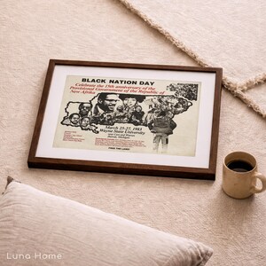 May include: A framed print with the text "BLACK NATION DAY" and "Celebrate the 15th anniversary of the Provisional Government of the Republic of New Afrika." The print is in a dark brown frame and rests on a beige surface. A mug of coffee sits nearby.