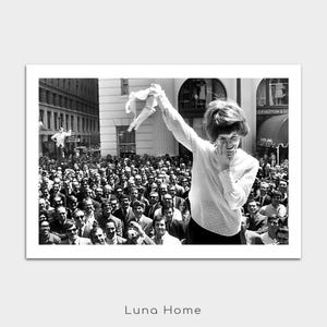 Puede incluir: Fotograf&iacute;a en blanco y negro de una mujer sonriendo y saludando a una multitud. Lleva una blusa blanca y una falda negra. La multitud est&aacute; compuesta por hombres con trajes. Impresi&oacute;n de Luna Home.