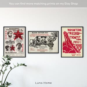 May include: Three framed posters with black frames hang on a white wall. The posters feature text and images in red, black, and white. One poster reads "Revolutionary Intercommunal Day of Solidarity for Bobby Seale." Another says "Black Nation Day." The third poster says "You Can't Jail the Revolution."