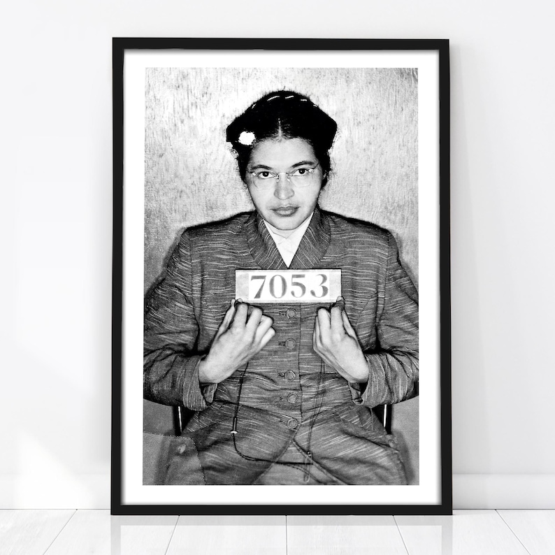 Black-and-white arrest photograph of Rosa Parks seated in a striped suit and holding police identification number 7053, associated with her refusal to surrender her bus seat and the historic Montgomery Bus Boycott.