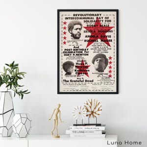 Pu&ograve; includere: Un poster incorniciato con bordo nero presenta testo e ritratti di personaggi politici. Il testo del poster include "Revolutionary Intercommunal Day of Solidarity" e "Huey P. Newton". Il poster ha un'estetica vintage con stelle rosse e sfondo crema.