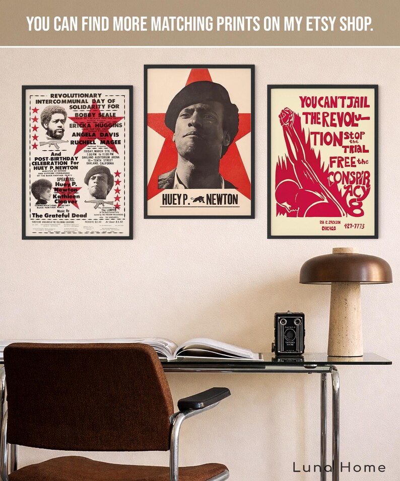 Pu&ograve; includere: Tre poster incorniciati con cornici nere sono esposti su un muro. I poster presentano testo e immagini di personaggi politici. Un poster ha il testo "Huey P. Newton". Una scrivania con una lampada e una fotocamera &egrave; di fronte ai poster.