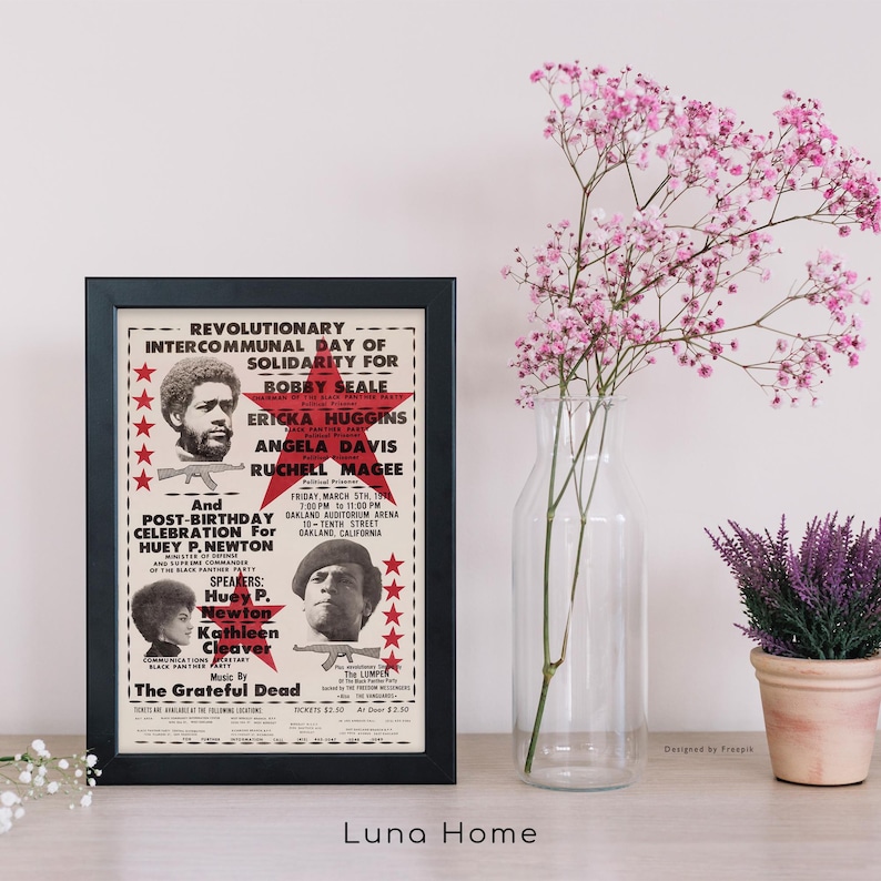 Pu&ograve; includere: Un poster incorniciato con un bordo nero, con testo e immagini relative a un evento politico. Il poster include ritratti di diverse persone e il testo "Giornata Intercomunale Rivoluzionaria di Solidariet&agrave;". Un vaso di fiori rosa e una pianta in vaso sono anche nell'immagine.