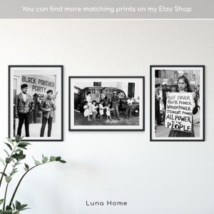 May include: Three framed black and white prints displayed on a white wall. The prints depict historical images, including a Black Panther Party gathering, a group of people near a vehicle, and a person holding a sign with the text "GAY POWER, BLACK POWER, WOMEN POWER, STUDENT POWER, ALL POWER TO THE PEOPLE."