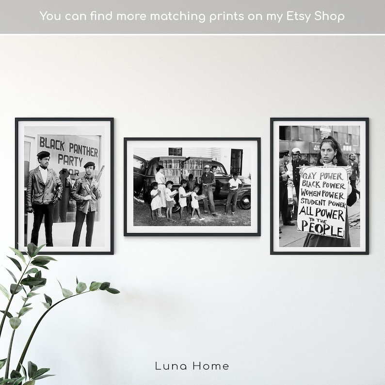May include: Three framed black and white prints displayed on a white wall. The prints depict historical images, including a Black Panther Party gathering, a group of people near a vehicle, and a person holding a sign with the text "GAY POWER, BLACK POWER, WOMEN POWER, STUDENT POWER, ALL POWER TO THE PEOPLE."