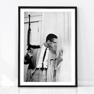May include: Black and white framed print featuring a man in a suit holding a rifle. The man is wearing glasses and a tie, looking out a window. The image is a portrait, with a focus on the man and the weapon.