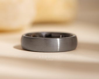 May include: A brushed gray tungsten carbide wedding band. The band has a simple, classic design and a smooth, matte finish.