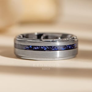 May include: A silver ring with a brushed metal finish and a band of deep blue, textured material. The ring has a wide band design, possibly a wedding band or fashion ring. The Redwood Rings logo is visible at the bottom.
