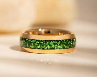 Könnte beinhalten: Ein goldfarbener Ring mit einem Band aus leuchtend grünen Steinen. Der Ring hat eine polierte Oberfläche und ein modernes Design. Der Text "REDWOOD RINGS" ist unten im Bild zu sehen.