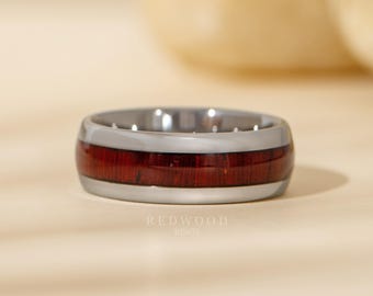 May include: A silver ring featuring a dark red wood inlay. The ring has a polished finish and the text "REDWOOD RINGS" is visible. The ring is shown in close-up on a neutral background.