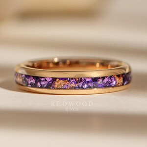 Op de afbeelding: Een gouden ring met een paarse en gouden inleg. De ring is simpel van ontwerp met een dunne band en een smalle inleg.