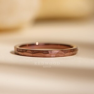 May include: A rose gold hammered wedding band. The band is thin and has a matte finish.