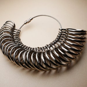 May include: A silver ring sizer with multiple rings of different sizes. The rings are connected by a silver chain.