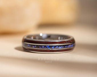 May include: A close-up of a ring with a silver band, featuring a dark wood inlay and a vibrant blue stone. The ring has a polished finish and the text "REDWOOD RINGS" is visible.