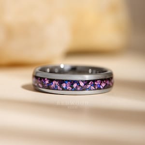 May include: A silver ring with a band filled with crushed purple and blue stones. The ring has a polished finish and the text "REDWOOD RINGS" is visible at the bottom.