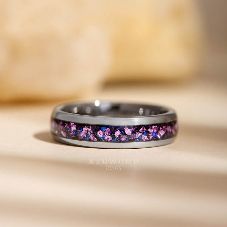 May include: A silver ring with a band filled with crushed purple and blue stones. The ring has a polished finish and the text "REDWOOD RINGS" is visible at the bottom.