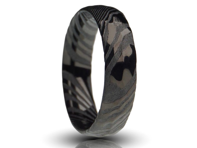 May include: A ring with a unique pattern of black, gray, and white swirls. The ring's design features a marbled effect, with the colors blending together to create a distinctive look. The ring is a band style, with a smooth, polished finish.