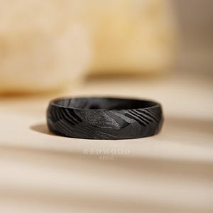 May include: A black ring with a textured surface and a unique pattern. The ring is made by Redwood Rings. The ring's design features a series of diagonal lines and a dark, matte finish, creating a modern and stylish look.