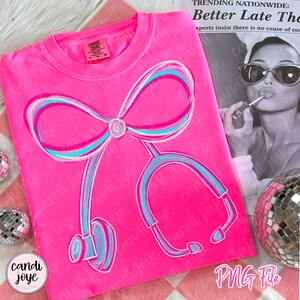 May include: A bright pink t-shirt featuring a stethoscope design with a bow at the top. The stethoscope is outlined in white, with blue and teal accents. The shirt has a crew neck and long sleeves. The text "PNG File" is visible in the bottom right corner.