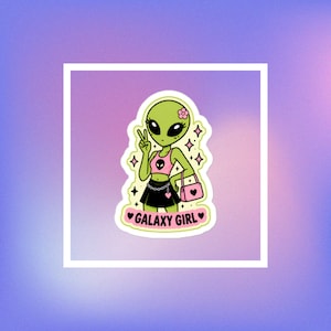 Op de afbeelding: Een gestanste sticker met een groen alien-personage met een roze bloem in het haar, gekleed in een roze crop top met een alien-gezicht icoon, een zwarte rok met een kettingriem en een roze handtas. De tekst GALAXY GIRL staat eronder gedrukt.