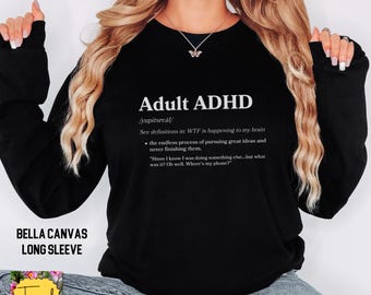 May include: Black long-sleeved sweatshirt with the words "Adult ADHD" and a definition printed in white. The sweatshirt also has the text "BELLA CANVAS LONG SLEEVE" and a small logo. The design is on the front of the shirt.