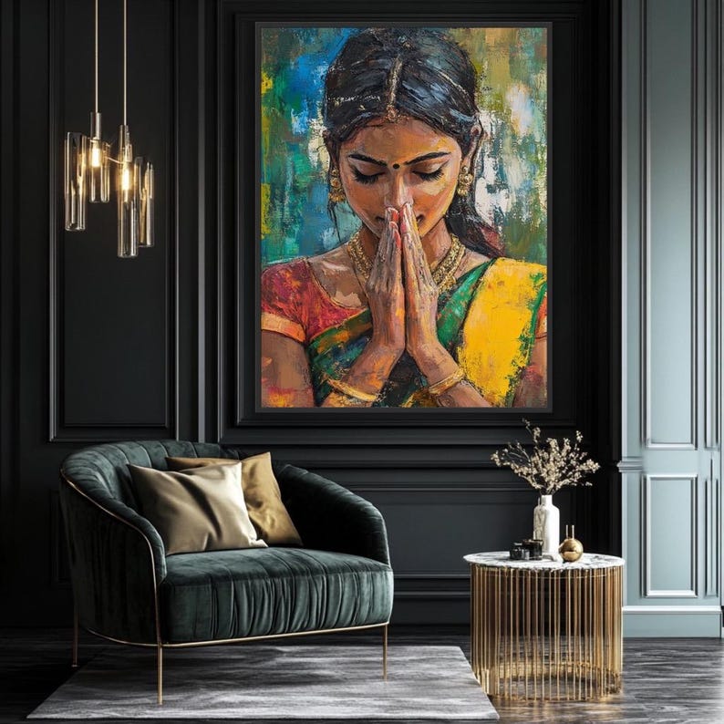 Indian wall art May include: An oil painting of a woman in traditional Indian attire, with hands clasped in prayer. The artwork features vibrant colors, including yellow, green, and red, set against a backdrop of blue and green brushstrokes. The painting is framed and displayed on a dark wall.