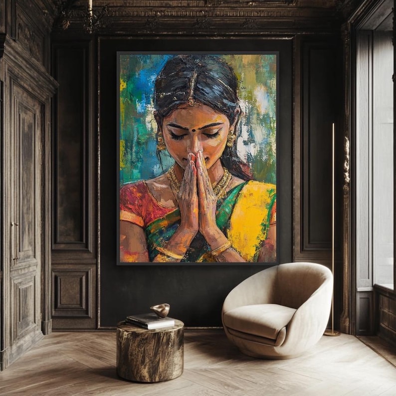 Indian wall art May include: An oil painting of a woman in traditional Indian attire, with hands clasped in prayer. The artwork features vibrant colors, including yellow, green, and red, and is framed in black. The painting hangs in a room with dark wood paneling and a modern chair.