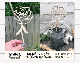 May include: A wooden cutout of a single flower with a stem. The flower is a simple, stylized design with rounded petals. The cutout is shown in two images, one with a hand holding it and the other with the cutout placed in a small metal pitcher. The text "Digital SVG files for Glowforge lasers" and "Difficulty level: beginner" is also shown in the image.
