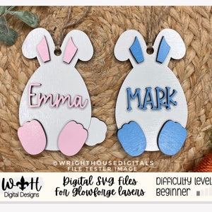 May include: Two white wooden bunny-shaped ornaments with pink and blue ears and feet. The ornaments are personalised with the names "Emma" and "Mark" in pink and blue lettering.