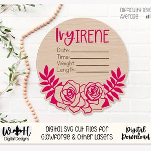 Könnte beinhalten: Ein rundes Holzschild mit dem Namen "Ivy Irene" und Platz zum Ausfüllen von Datum, Uhrzeit, Gewicht und Länge. Das Schild ist mit rosa Rosen und Blättern verziert.