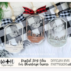 Może przedstawiać: Trzy białe drewniane ozdoby o zimowym motywie. Każda ozdoba przedstawia księżyc, drzewa i inne świąteczne pozdrowienia. Ozdoby są ozdobione czarno-białą wstążką w kratę buffalo i białą drewnianą koralikiem.