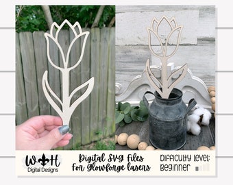 May include: A light-colored wooden tulip cut-out. The tulip is displayed in a galvanized metal container. The image also includes the text "Digital SVG files for Glowforge lasers" and "Difficulty level: Beginner".