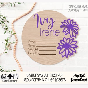 Könnte beinhalten: Ein Holz-Kreis mit dem Namen "Ivy Irene" in lila Schrift. Der Kreis hat Linien zum Aufzeichnen von Datum, Uhrzeit, Gewicht und Länge. Zwei lila Blumenmuster befinden sich auf der rechten Seite des Kreises. Der Hintergrund ist eine weiße Backsteinwand.