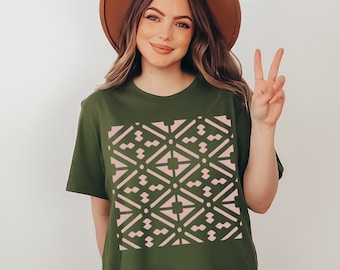 Puede incluir: Camiseta verde oliva con un patrón geométrico rosa. El diseño presenta un patrón repetitivo de formas de diamante y pequeños círculos. La camiseta es de estilo casual.