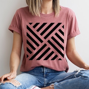 May include: A woman wearing a dusty rose t-shirt with a black geometric pattern. The pattern is made up of diagonal lines that intersect to form a grid.