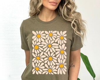 Puede incluir: Una camiseta verde de manga corta con un estampado gráfico de un patrón de margaritas blancas con centros amarillos.