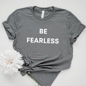 May include: A grey t-shirt with the text "BE FEARLESS" printed in white on the front.