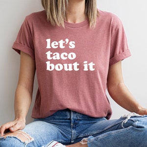 May include: A mauve t-shirt with the text "let's taco bout it" in white.