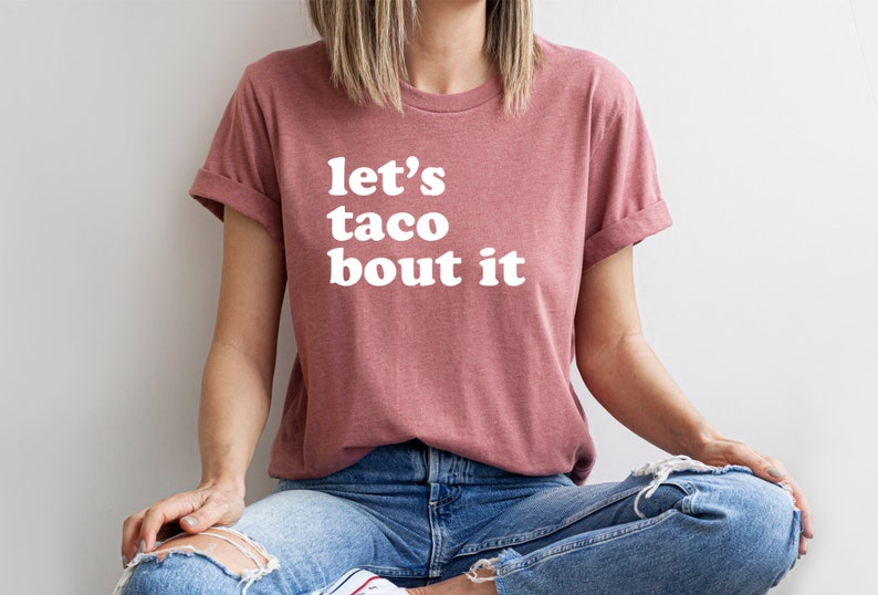 May include: A mauve t-shirt with the text "let's taco bout it" in white.