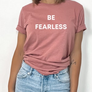 May include: A pink t-shirt with the text "BE FEARLESS" printed in white on the front.