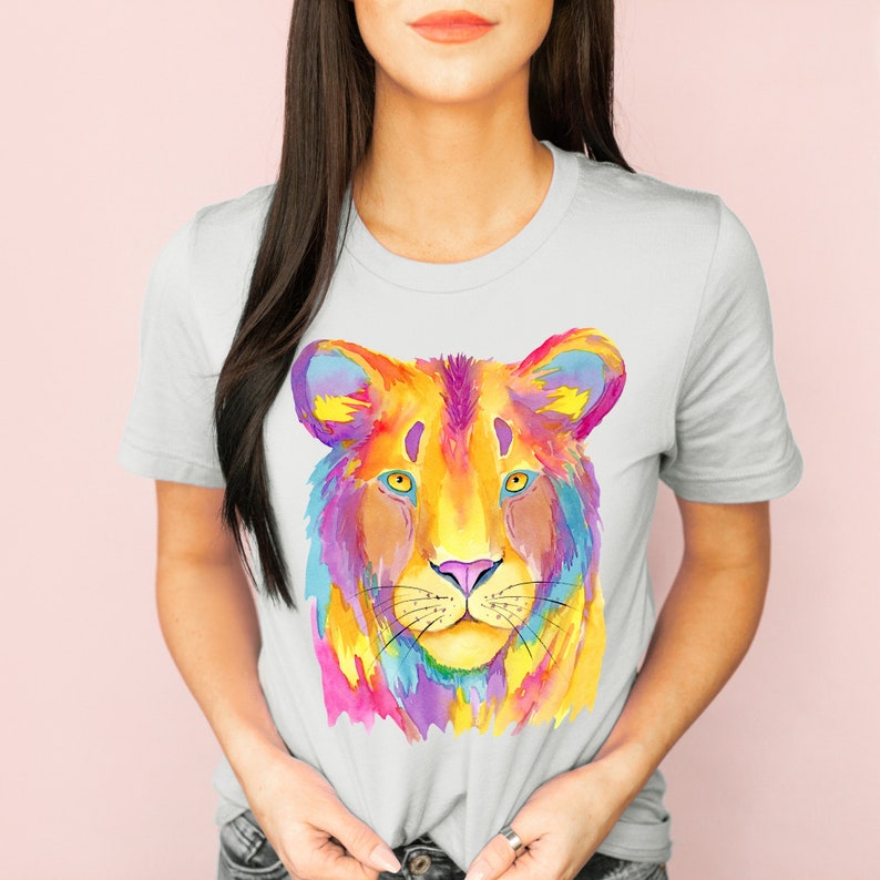May include: A white t-shirt with a colorful watercolor illustration of a lion's face. The lion's fur is painted in shades of yellow, orange, pink, purple, and blue.
