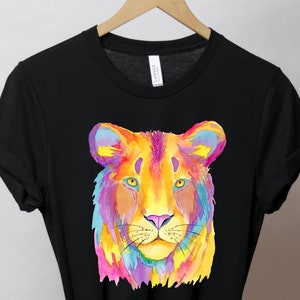 May include: A black t-shirt with a colorful watercolor illustration of a lion's face. The lion's fur is painted in shades of pink, yellow, orange, blue, and purple.