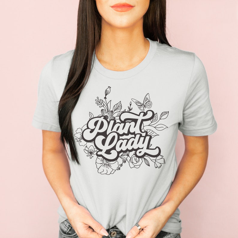 May include: A white t-shirt with a black and white graphic design featuring the text "Plant Lady" surrounded by stylized flowers and a butterfly.
