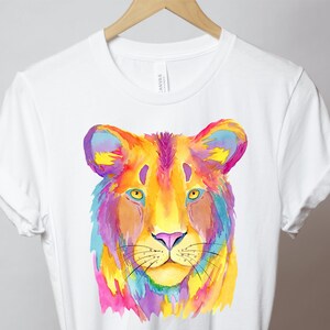 May include: A white t-shirt with a colorful watercolor illustration of a lion's face. The lion's fur is painted in shades of yellow, orange, pink, purple, and blue.