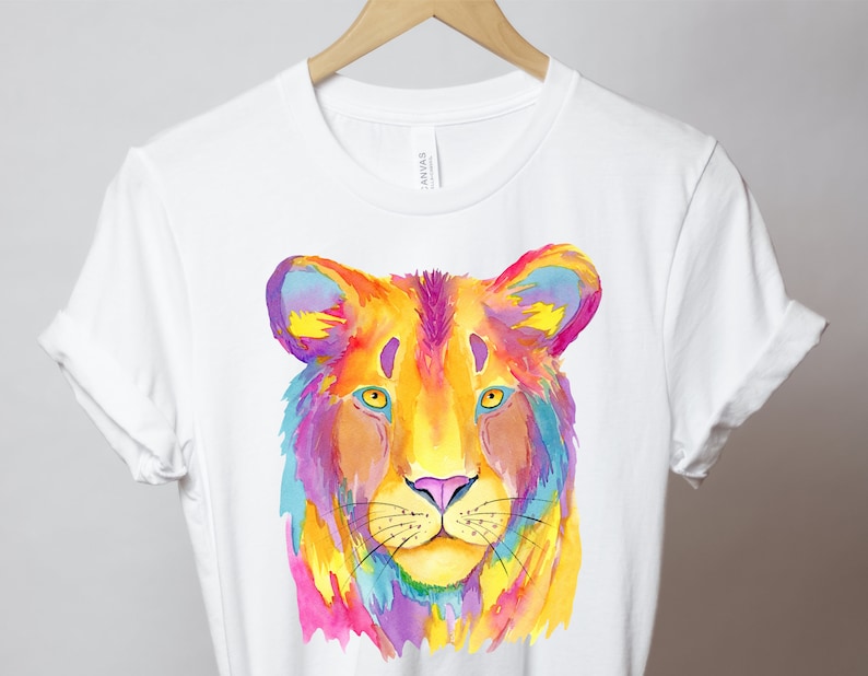 May include: A white t-shirt with a colorful watercolor illustration of a lion's face. The lion's fur is painted in shades of yellow, orange, pink, purple, and blue.