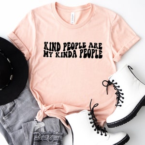 May include: A peach-colored t-shirt with the text "Kind people are my kinda people" in black retro-style lettering.