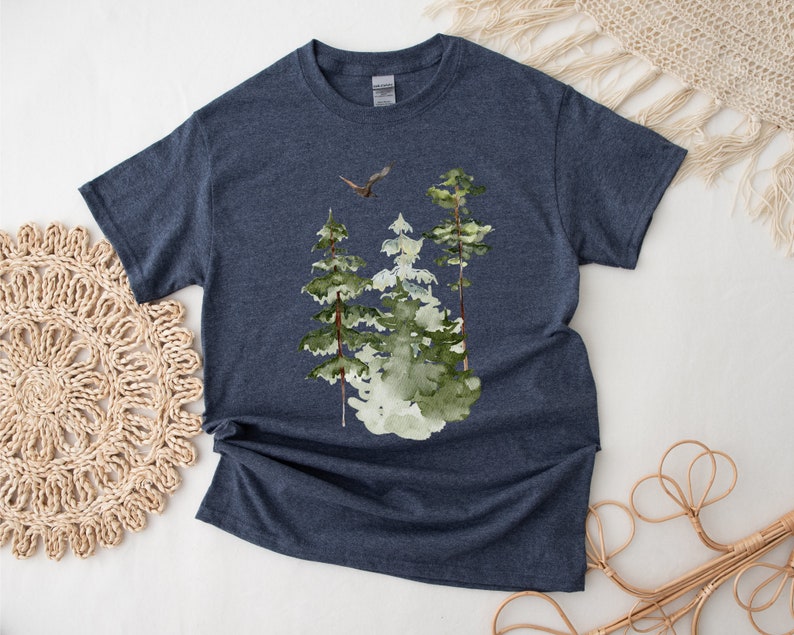 May include: A navy blue t-shirt with a watercolor design of three green trees and a bird flying above them.
