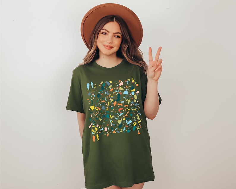 Pu&ograve; includere: Una maglietta verde con un motivo a coriandoli colorati. La maglietta ha una vestibilit&agrave; rilassata e un collo rotondo.