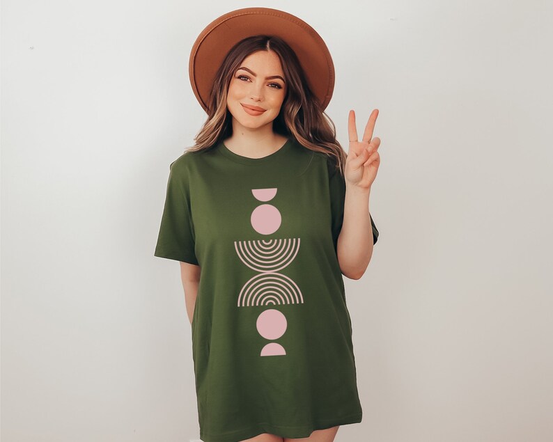 May include: A green t-shirt with a pink and brown geometric design. The design features a series of circles, half-circles, and arcs stacked vertically.